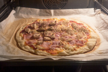 Handmade mushroom and ham pizza, with melted cheese and tomato sauce, baking in the oven on parchment paper