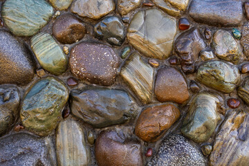 A texture of smooth, wet stones of different sizes, shapes and colours, tightly packed together.