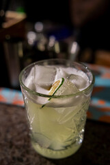 A glass of gin based Basil Smash cocktail on bar. Closeup cocktail glass.Blurry background. Basil smash alcoholic cocktail drink with dry gin, syrup, lemon, basil and ice, dark bar counter background.