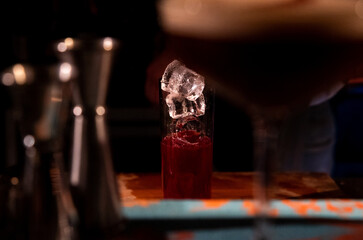 Cocktail glass with ice on top, red drink, vodka, espresso martini blurred glass, bar accessories. Sophisticated drink, alluring presentation. Alcoholic cocktail drink with ice cubes, red drink.