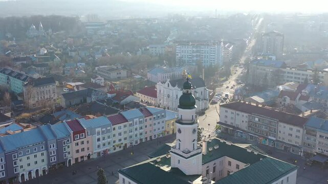 A quadcopter captures a stunning panorama of Drohobych, Ukraine, focusing on the central square where a historic town hall stands proudly. The video highlights the town's charm and rich heritage from