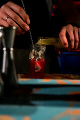 Bartender mixing alcoholic cocktail drink with ice cubes. Bartender hands pouring beverage. Man fingers. Cocktail glass with ice on top, red drink, vodka, glass, bar accessories. Sophisticated drink.