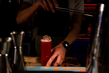 Bartender mixing alcoholic cocktail drink with ice cubes. Bartender hands pouring beverage. Man fingers. Cocktail glass with ice on top. Pouring soda in a cocktail glass. Ring man hands