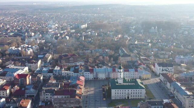 A quadcopter captures a stunning panorama of Drohobych, Ukraine, focusing on the central square where a historic town hall stands proudly. The video highlights the town's charm and rich heritage from