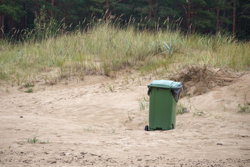 green garbage can in the sand of the sea beach