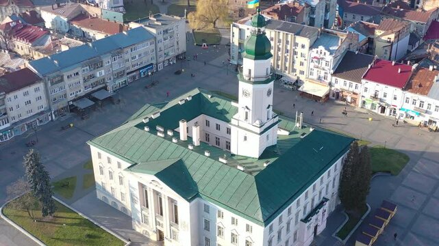 A quadcopter captures a stunning panorama of Drohobych, Ukraine, focusing on the central square where a historic town hall stands proudly. The video highlights the town's charm and rich heritage from