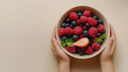 Overhead view of hands holding bowl full of fresh berries,  raspberries, blueberries, strawberries, and mint