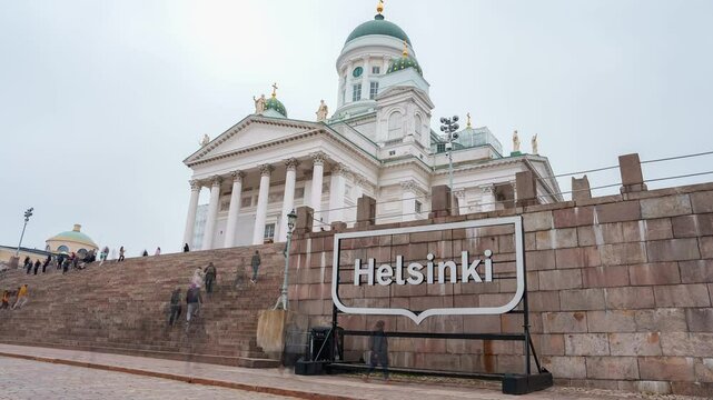 Helsinki Cathedral's neoclassical architecture and green domes stand out as people move dynamically on the steps, with an overcast sky above.