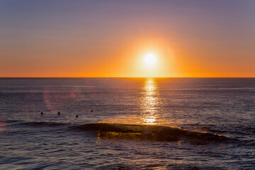 Surfers in the ocean with sunrise in the horizon and a breaking wave. Gold Coast, Australia