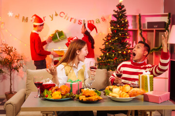 Lively New Year Eve and christmas party Asian friends and colleagues of various ages celebrating together. Champagne, wine, gift boxes, festive decorations create a warm, joyful holiday atmosphere.