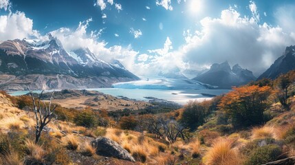 Scenic image of deep blue glacial lake with mountains, red foliage, snow-capped peak, and yellow grass under bright sky. Rich in color and natural beauty.