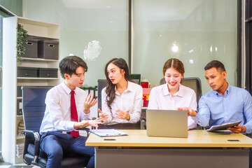 In a professional office setting, two men and two women, boss and subordinates, celebrate reaching business target. They sit together, smiling, laptops and desks, sharing success and congratulations.