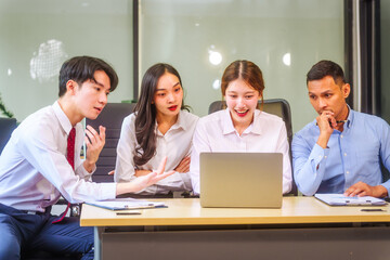In a professional office setting, two men and two women, boss and subordinates, celebrate reaching business target. They sit together, smiling, laptops and desks, sharing success and congratulations.