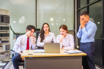 Two men and two women, including boss and employees, discuss recent mistake. Expressions of disappointment and constructive criticism create a tense, reflective atmosphere around laptops and desks.