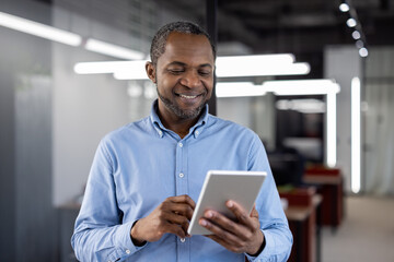 Confident mature African American businessman holding tablet in modern office environment. Smiling...