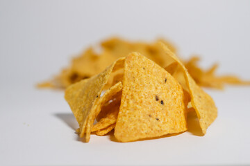 The chips have a triangular shape with a rough texture and small black seasoning specks visible on the surface. They appear crispy and ready to eat, with some chips overlapping each other. 