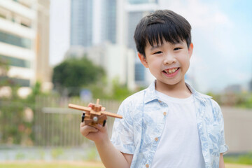 A cheerful young boy holds a model airplane in the park, beaming with excitement and imagination on a bright, sunny day, capturing the spirit of childhood play and adventure.