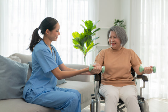 Compassionate caregiver assists elderly woman with home workout using dumbbells, promoting health, happiness, and wellness in retirement. Supportive senior care and exercise.