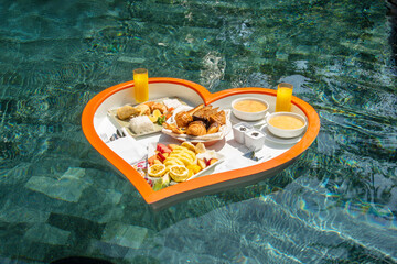 Floating heart-shaped plate with a breakfast of fruits, rice, fish, buns, juice  in the swimming pool in the Maldives