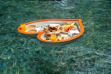 Floating heart-shaped plate with a breakfast of fruits, rice, fish, buns, juice  in the swimming pool in the Maldives