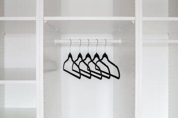 Dark black velvet hangers without clothes on rail into white empty wardrobe at home. Closeup. Front...