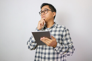 young asian man holding a tablet and looking in tablet screen with a confused gesture of another hand isolated over a plane white background