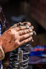 Dirty and calloused hands of a mechanic assembling compressed coil spring during DIY car repairs. Closeup.