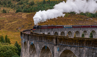 Naklejka premium Steam train at Glenfinnan Autumn in Scotland with reflections in the lochs