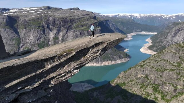 Girl on the edge of cliff on Trolltunga, Norway. Aerial Drone Shot, Norwegian Travel Highlight SIghtseeing Troll Tongue