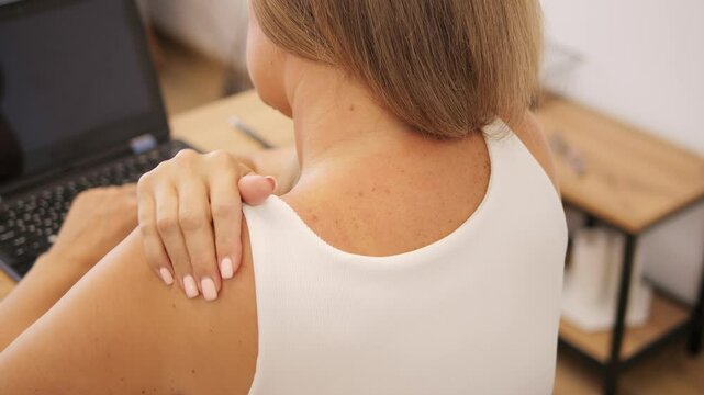 Woman feeling neck pain while working on laptop, adjusting her posture. The pain shows the strain from prolonged screen time. Ideal for themes of workplace discomfort, health, and managing neck pain.