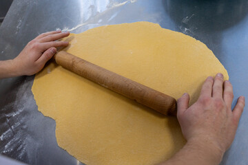 The cook's hands roll out the dough with a rolling pin on the production table