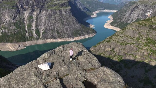 Adventurous Travelling Girl is Coming to the edge of cliff in Norwegian Mountains. Aerial Shot, Troll Tongue, Norway
