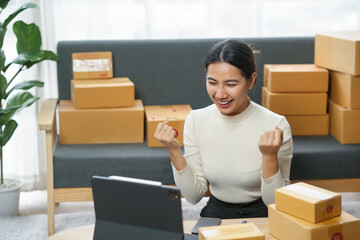 Excited woman celebrating success at home office with laptop and packages, symbolizing e-commerce and online business growth.