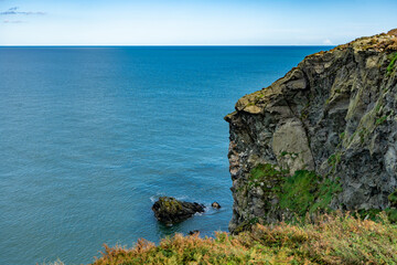 A cliff above the ocean on a sunny day, with water below and clouds in the sky