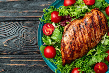 Grilled chicken breast ( fillet ) with lattuce salad and cherry tomatoes . Top view