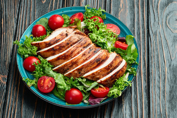 Grilled chicken breast ( fillet ) with lattuce salad and cherry tomatoes . Top view