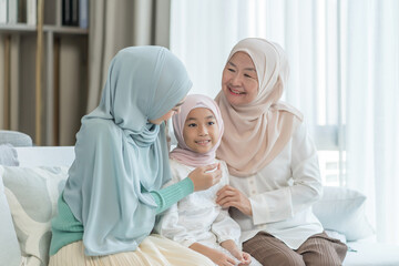 Obraz premium portrait of happy three different generations female muslim family meeting at home,sitting on couch in living room,gentle touching with love, smile,enjoy holiday time together