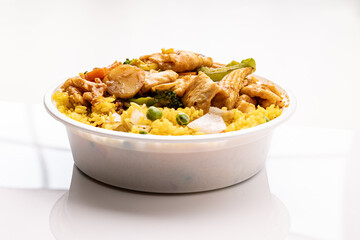 Traditional Szechuan chicken with vegetables, served in a plastic container with yellow fried rice from a Chinese restaurant’s takeout to go or delivery menu.