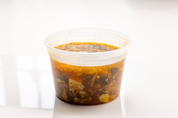 Hot and sour Asian soup in a plastic container, served as part of a lunch special for takeout or delivery from a Chinese restaurant.