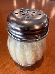A glass container full of Parmesan cheese with a silver top.