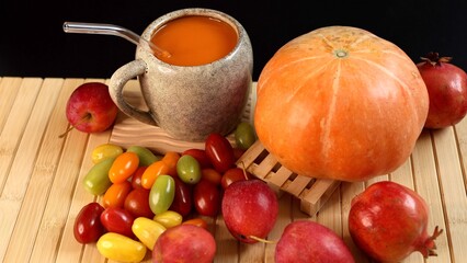 Pumpkin beside ceramic mug filled with pumpkin beverage, scattered fruits on bamboo surface, vibrant autumn harvest theme emphasized by rich organic textures, bright colors, and natural light.
