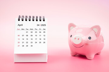 Desk calendar for April 2025 and pink piggy bank on pink background.