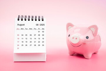 Desk calendar for August 2025 and pink piggy bank on pink background.