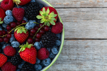 Mix of ripe colorful berries in bowl photography . Blueberry , strawberry , raspberry , blackberry and red currant . Top view