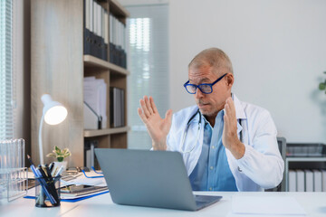 Senior male doctor gesturing and having video conference on laptop in medical office