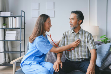 Young nurse using stethoscope examining senior man patient for checking heartbeat in living room at...