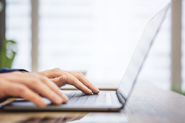 The image shows a close-up of a man's hands typing on a state-of-the-art laptop keyboard, with an office scene appearing blurry in the background