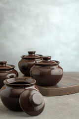 Dark clay baking pots on kitchen counter among vegetables