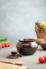 Dark clay baking pots on kitchen counter among vegetables