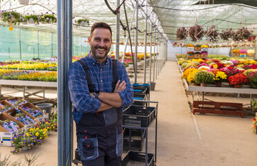Fototapeta premium Confident worker in greenhouse with colorful plants in background